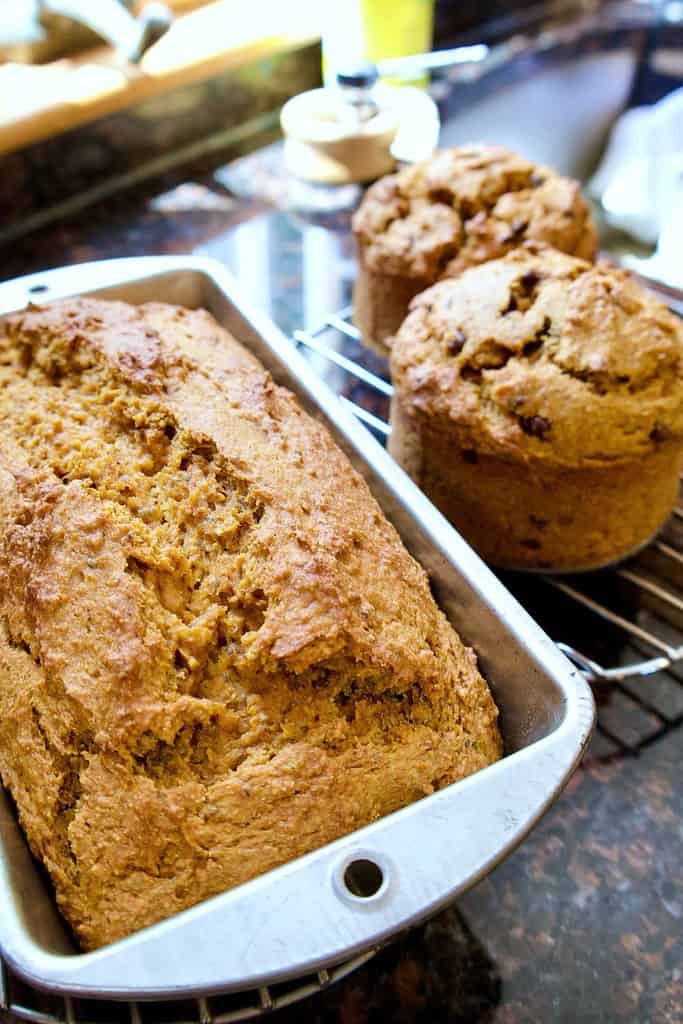 banana pumpkin bread in a loaf pan and muffins on a cooling rack