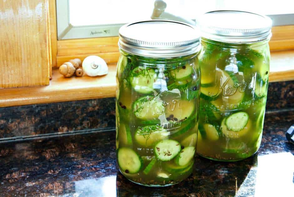 two-sealed-mason-jars-filled-sliced-pickled-cucumbers-next-to-windowsill