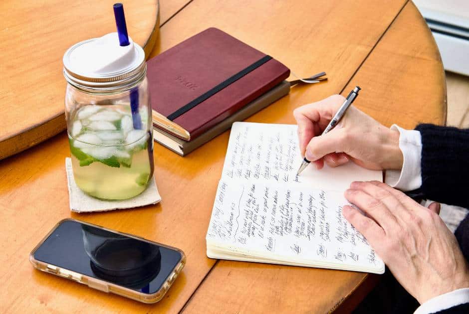 hands-writing-in-journal-mason-jar-mint-water-iphone-two-books