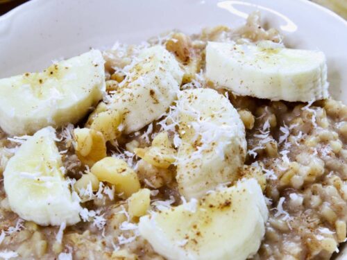 steel-cut-oatmeal-in-white-bowl-with-sliced-bananas-walnuts-cinnamon-shredded-coconut