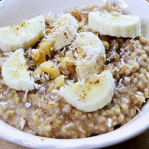 steel-cut-oatmeal-in-white-bowl-with-sliced-bananas-walnuts-cinnamon-shredded-coconut