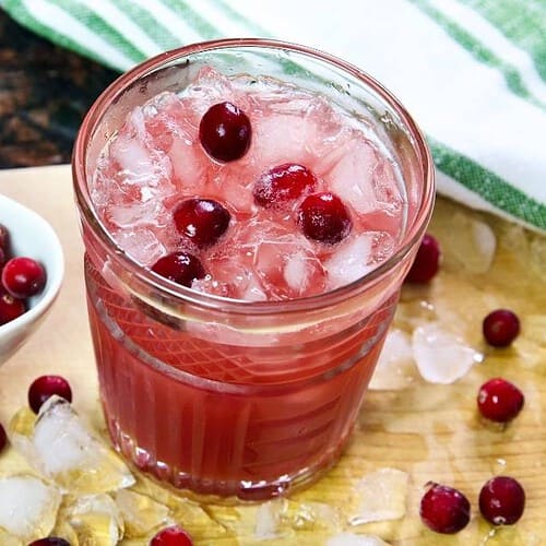 cranberry-mocktail-with-ice-and-a-small-bowl-of-fresh-cranberries-on-a-wooden-cutting-board