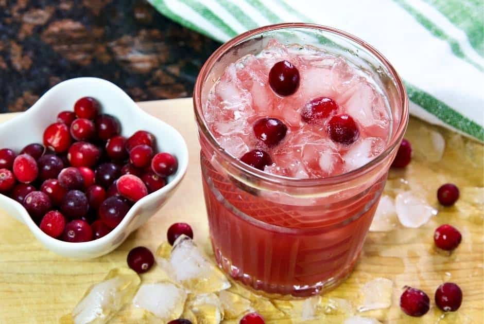 cranberry mocktail with ice and a small bowl of fresh cranberries on a wooden cutting board