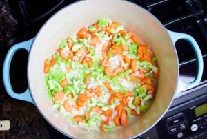 chopped onions celery and carrots in a dutch oven on the stove