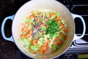 chopped garlic parsley onion carrots celery and herbs in a dutch oven on the stove