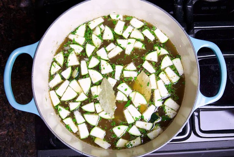 vegetable broth chopped zucchini parsley and bay leaves in a dutch oven on the stove