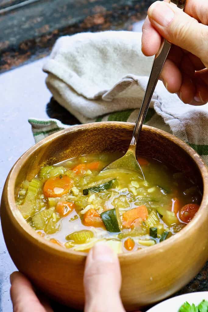 hands holding lemon and rice soup in a wooden bowl with spoon