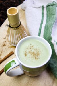 matcha latte in a cup with whisk and kitchen towel in background