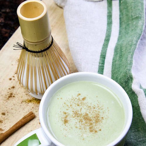 matcha latte in a cup with whisk and kitchen towel in background