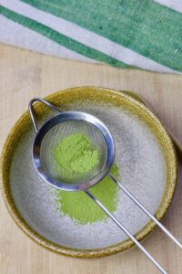 matcha powder sifting through a strainer into a bowl