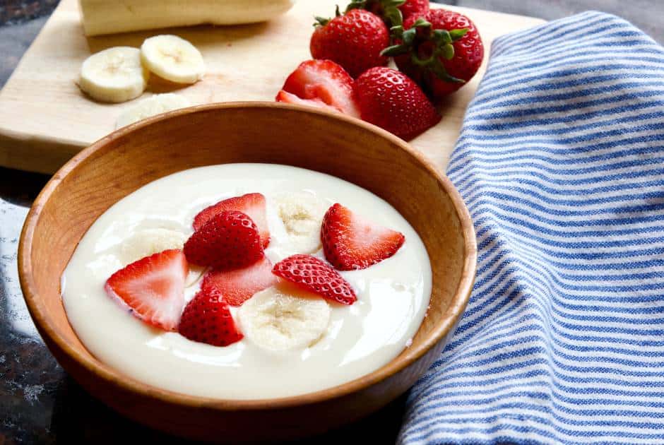 yogurt in a wooden bowl with fruit and striped kitchen towel on side