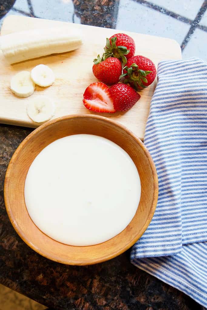 non-dairy yogurt in wooden bowl with fruit on a cutting board