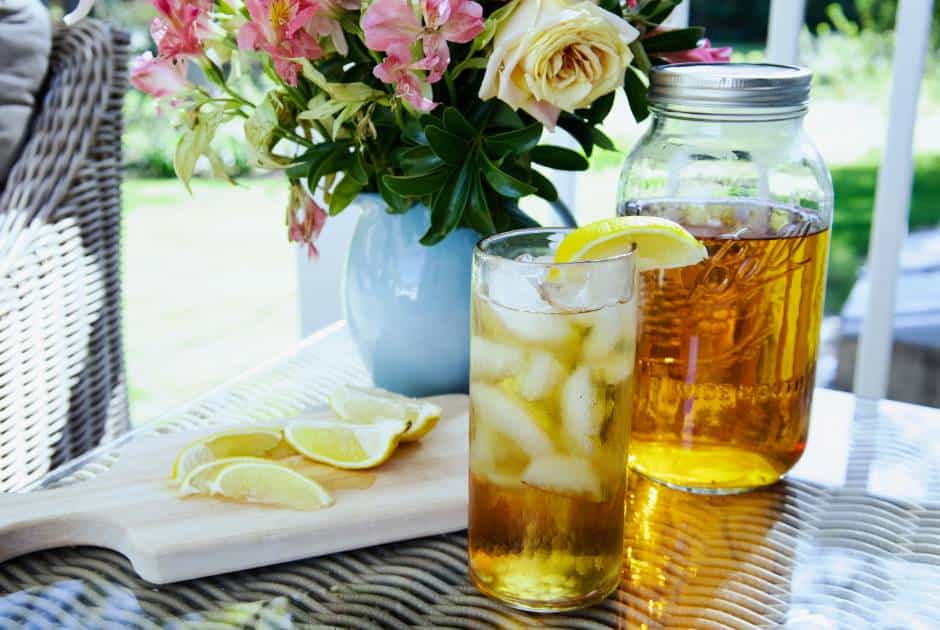 large glass of sun tea with mason jar, flowers, sliced lemons in the background
