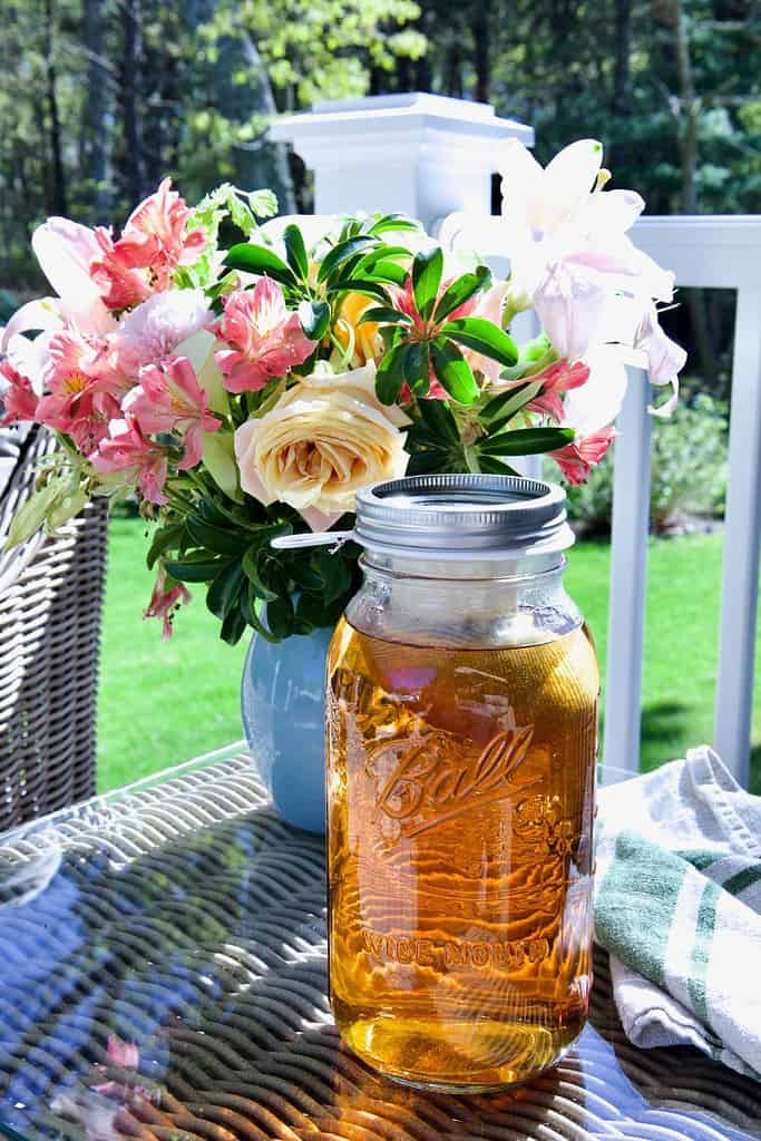 large mason jar filled with herbal sun tea sitting on a table outside with a vase of flowers in the background