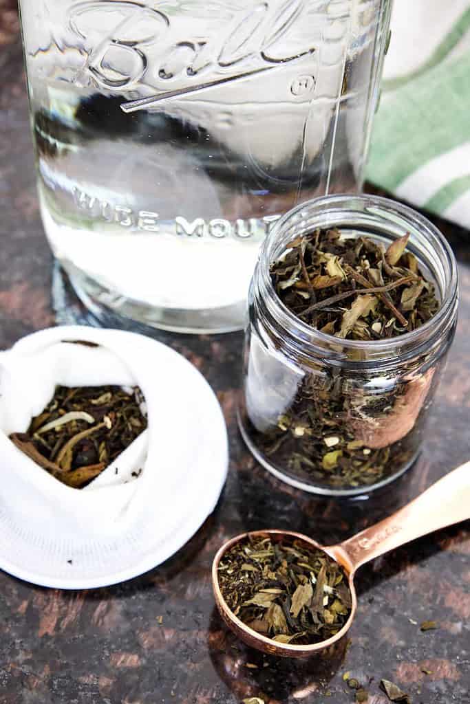 loose leaf herbal tea in small glass jar tablespoon holding dry tea tea filter on side mason jar in background