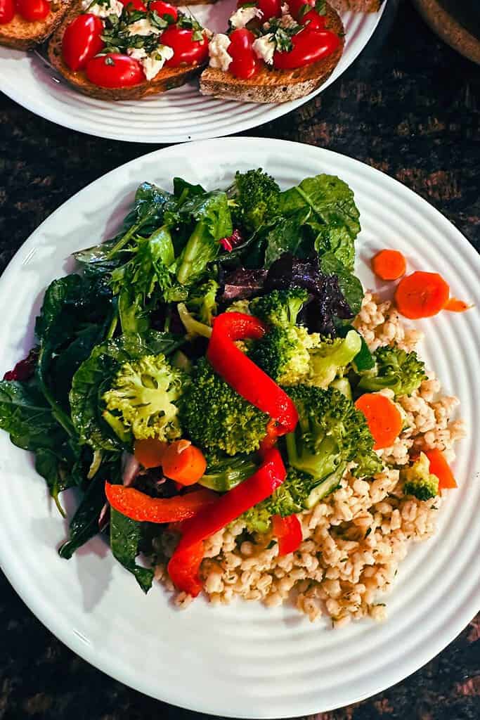 white plate with high fiber foods barley broccoli leafy greens sliced carrots red peppers