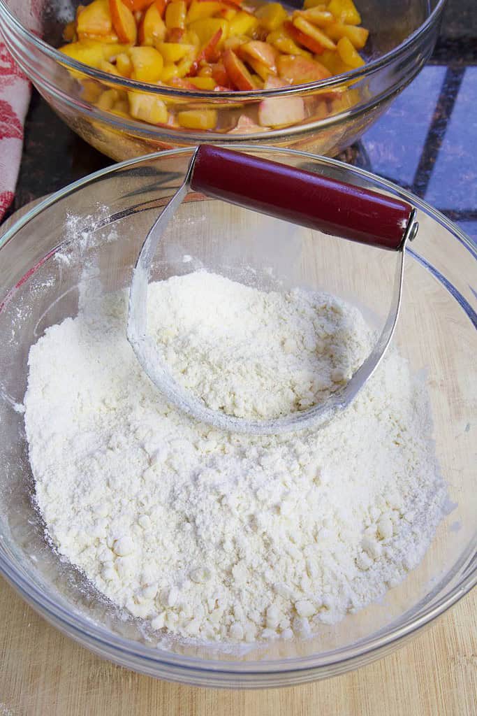 flour and sugar crumbled in a glass bowl with pastry cutter