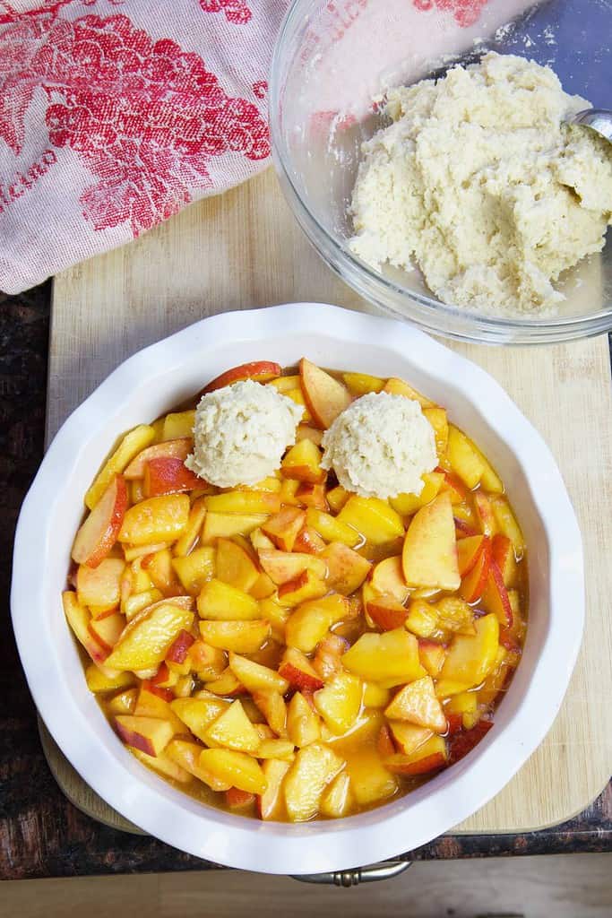 sliced peaches in a pie dish with dollops of biscuit dough on top