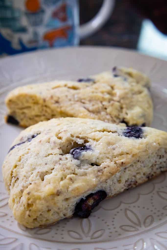 two blueberry scones on a plate with a coffee mug in the background