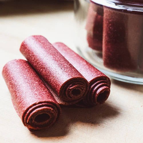 fruit leathers rolled in a glass jar and three on a cutting board