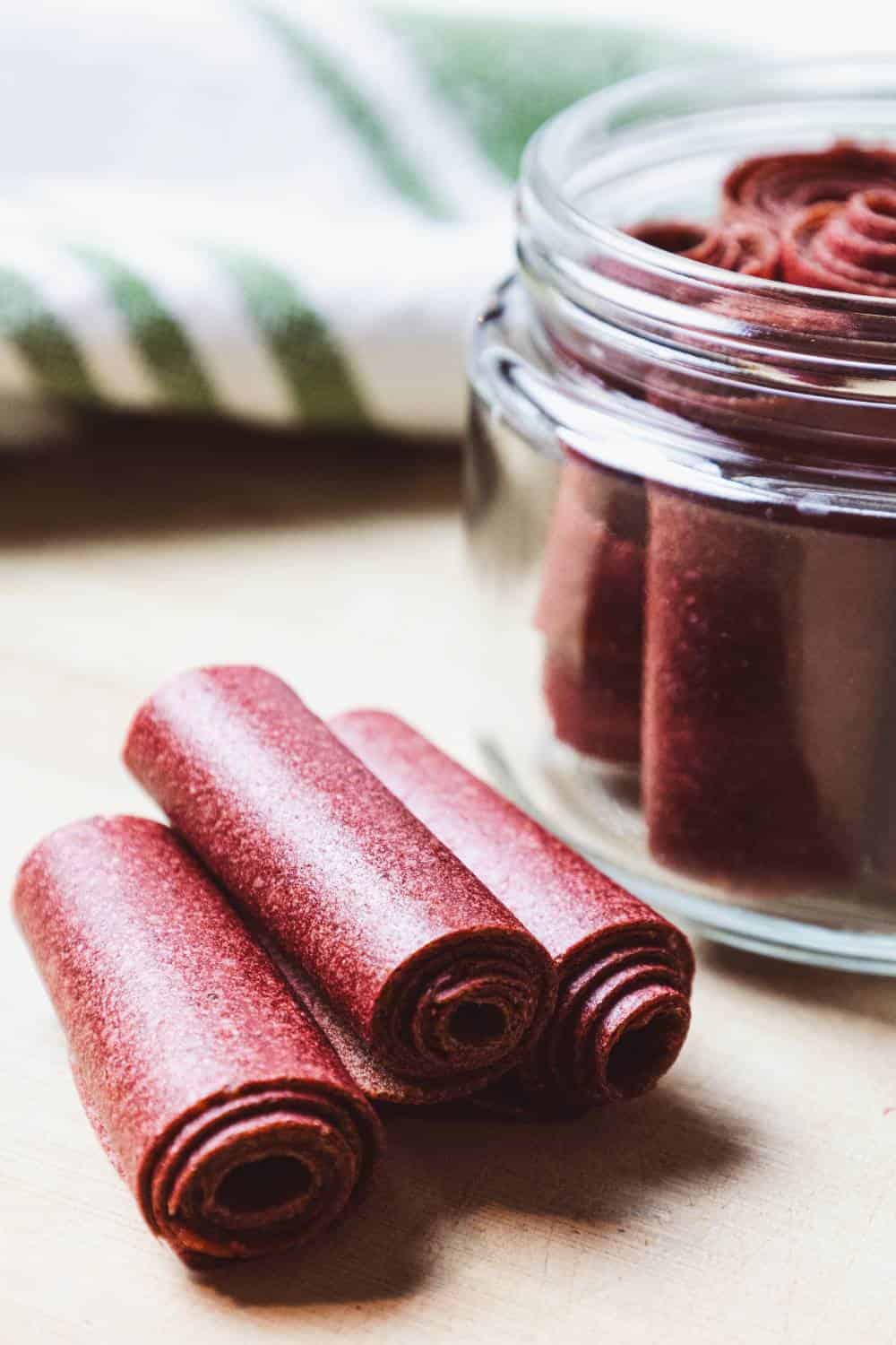 fruit leathers rolled in a glass jar and three on a cutting board