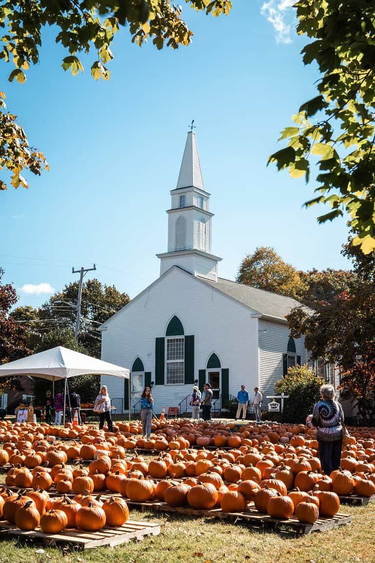 new england in the fall with a pumpkin patch in front of an old historic church