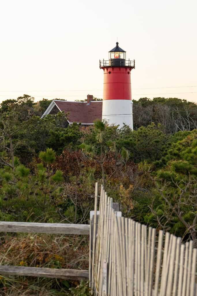 cape cod in autumn with a picket fence and a lighthouse in the background