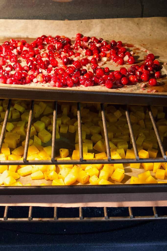 baking trays with cranberries and squash on racks in the oven