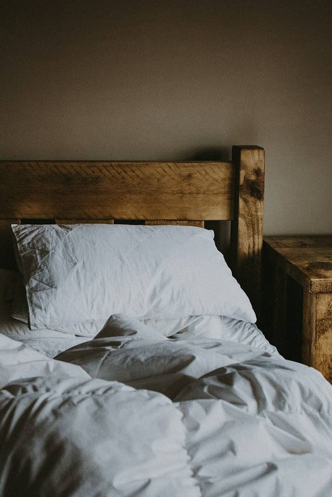 wood frame bed with white linens for a night routine schedule