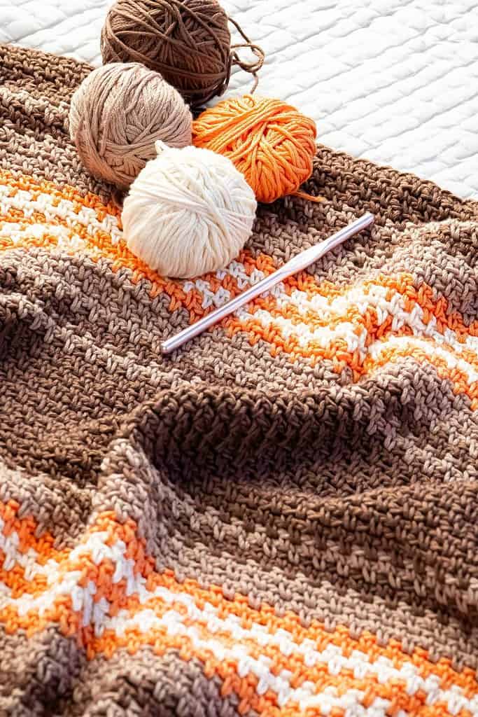 brown orange cream crocheted blanket with yarn balls and crochet hook