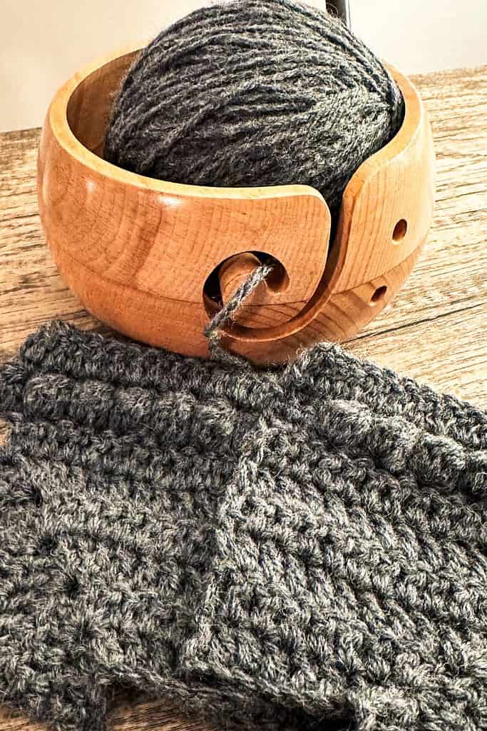 crochet baby grey sweater with ball of yarn in wood bowl