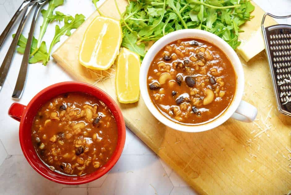 two cups of black bean vegan chili on a cutting board with lemon wedges and arugula greens