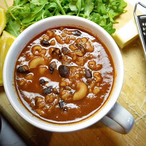 white bowl of black bean vegan chili with arugula greens in the background