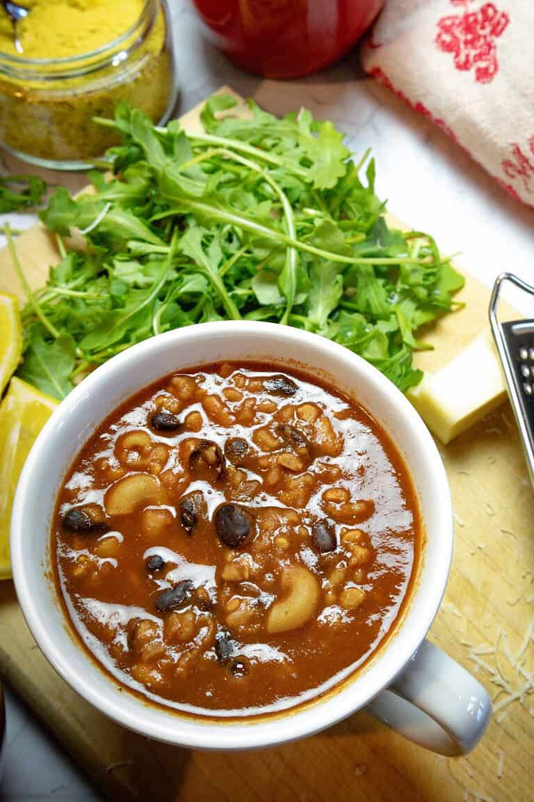 white bowl of black bean vegan chili with arugula greens in the background