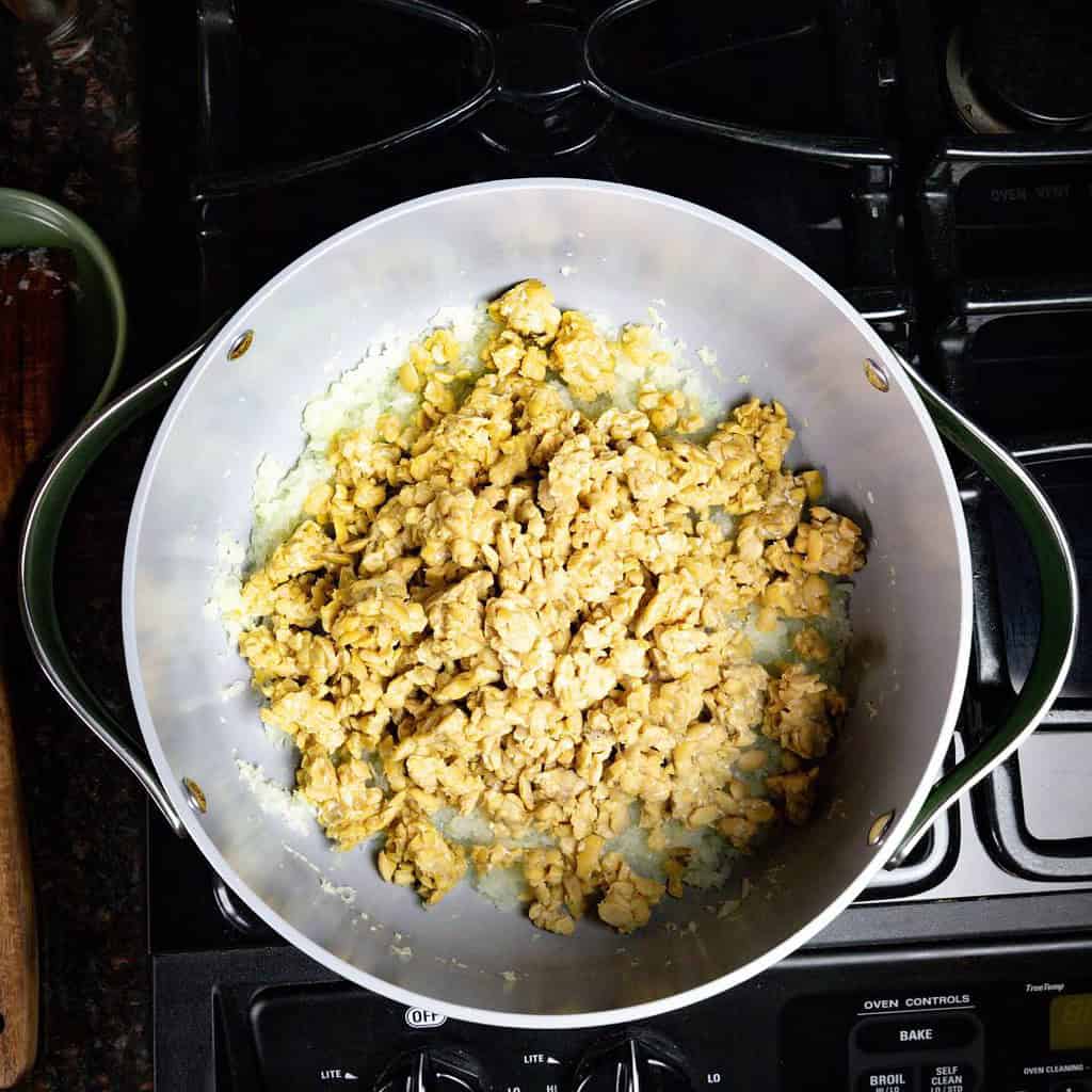 large pot on the stove with tempeh and diced onions