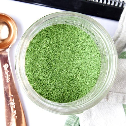 diy green powder in an open glass jar with a copper measuring teaspoon next to it