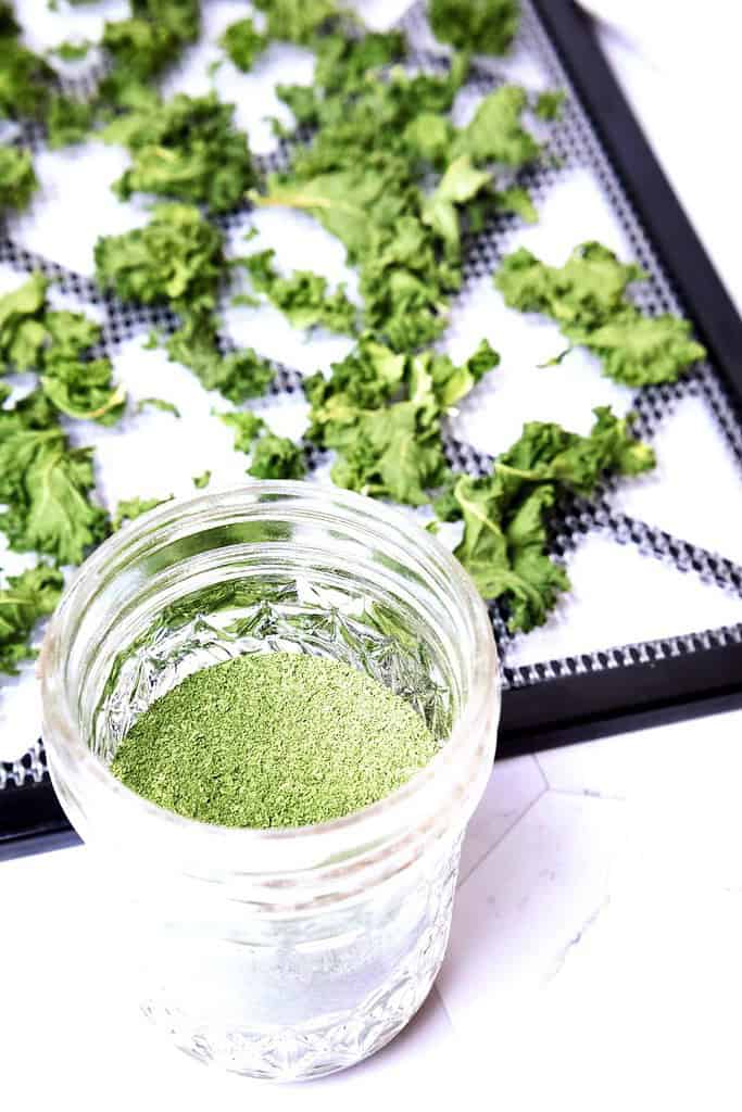 diy green powder in a small mason jar with a kale filled dehydrator tray in the background