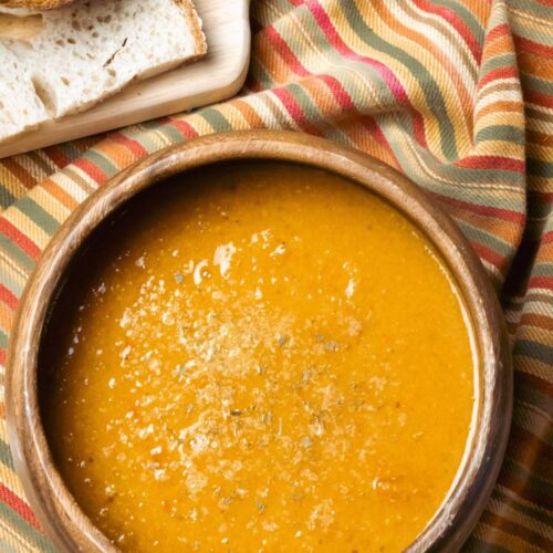 tomato lentil soup in a wooden bowl with slices of sourdough bread on a cutting board