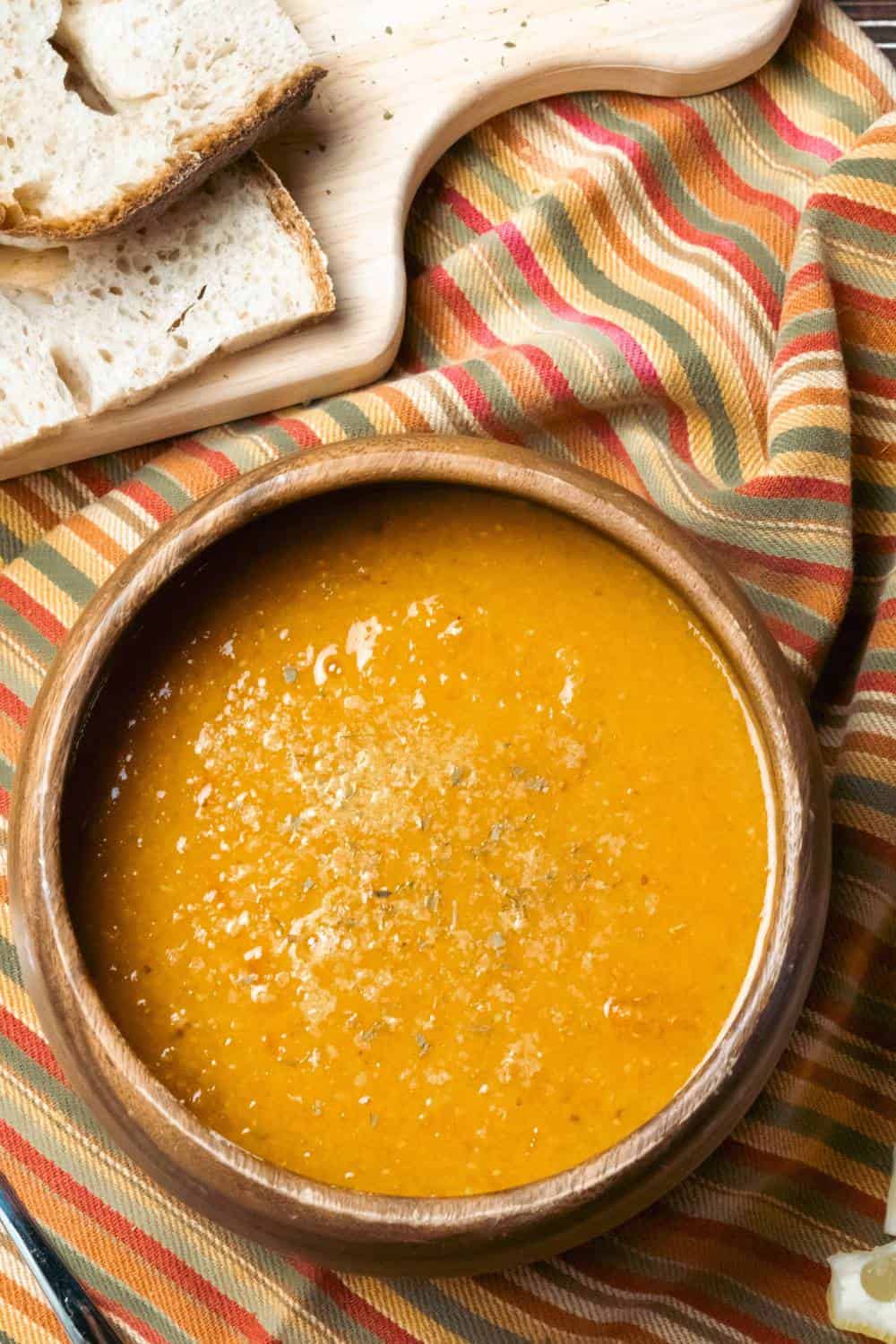 tomato lentil soup in a wooden bowl with slices of sourdough bread on a cutting board