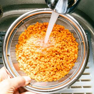 red lentils in a colander being rinsed in the sink with running water