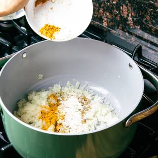 seasoning being added to a large soup pot with diced onions