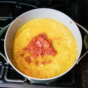 crushed tomatoes added to a large soup pot with tomato lentil soup