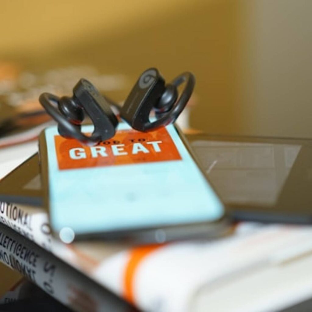 ear buds sitting on top of an iphone kindle and book