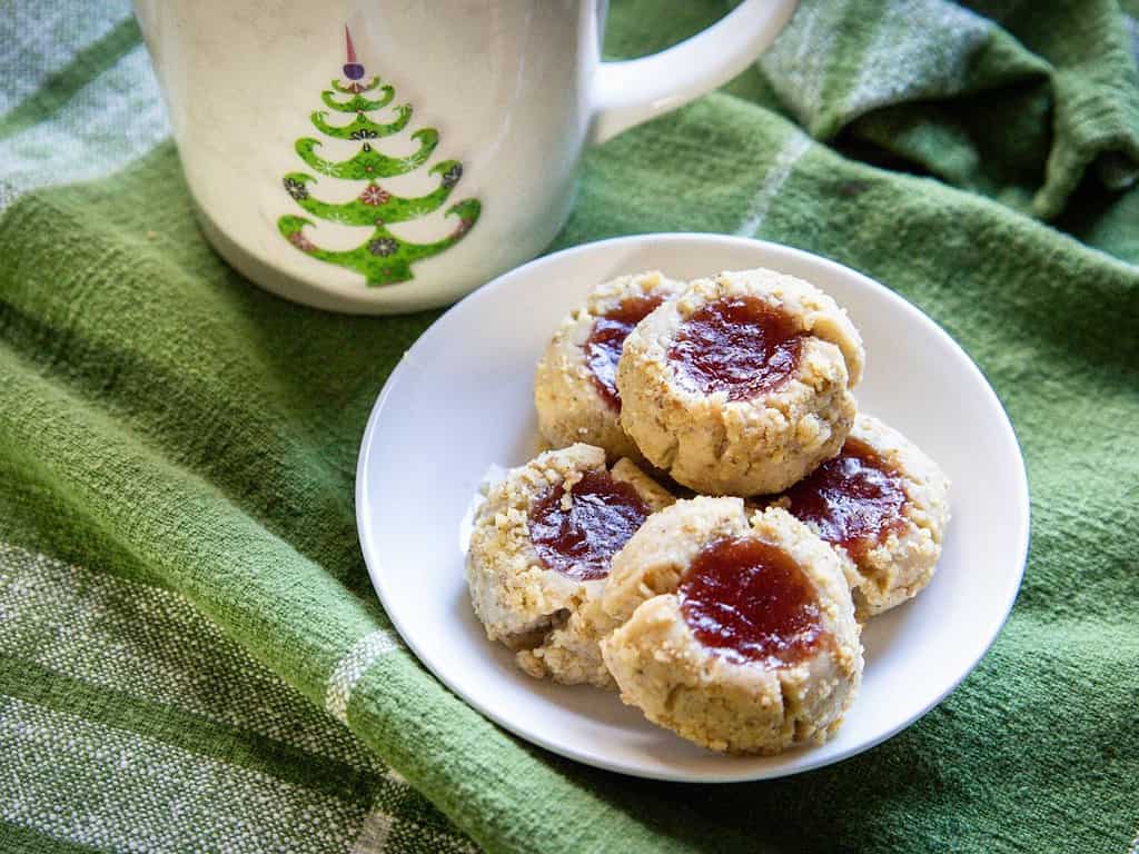 thumbprint cookies in a small white dish with a christmas mug behind it