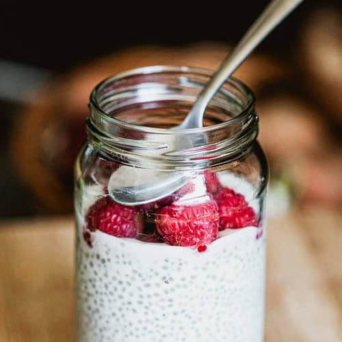 chia seed pudding in a mason jar topped with raspberries and a spoon