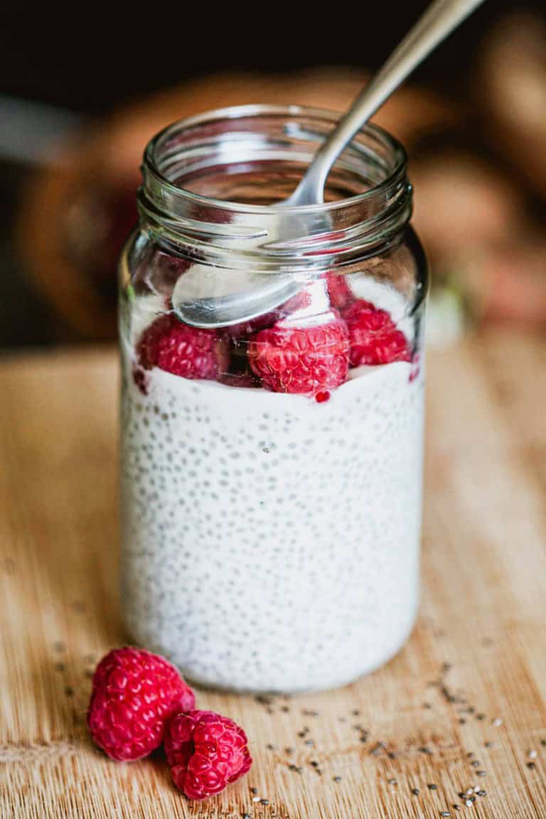 chia seed pudding in a mason jar topped with raspberries and a spoon